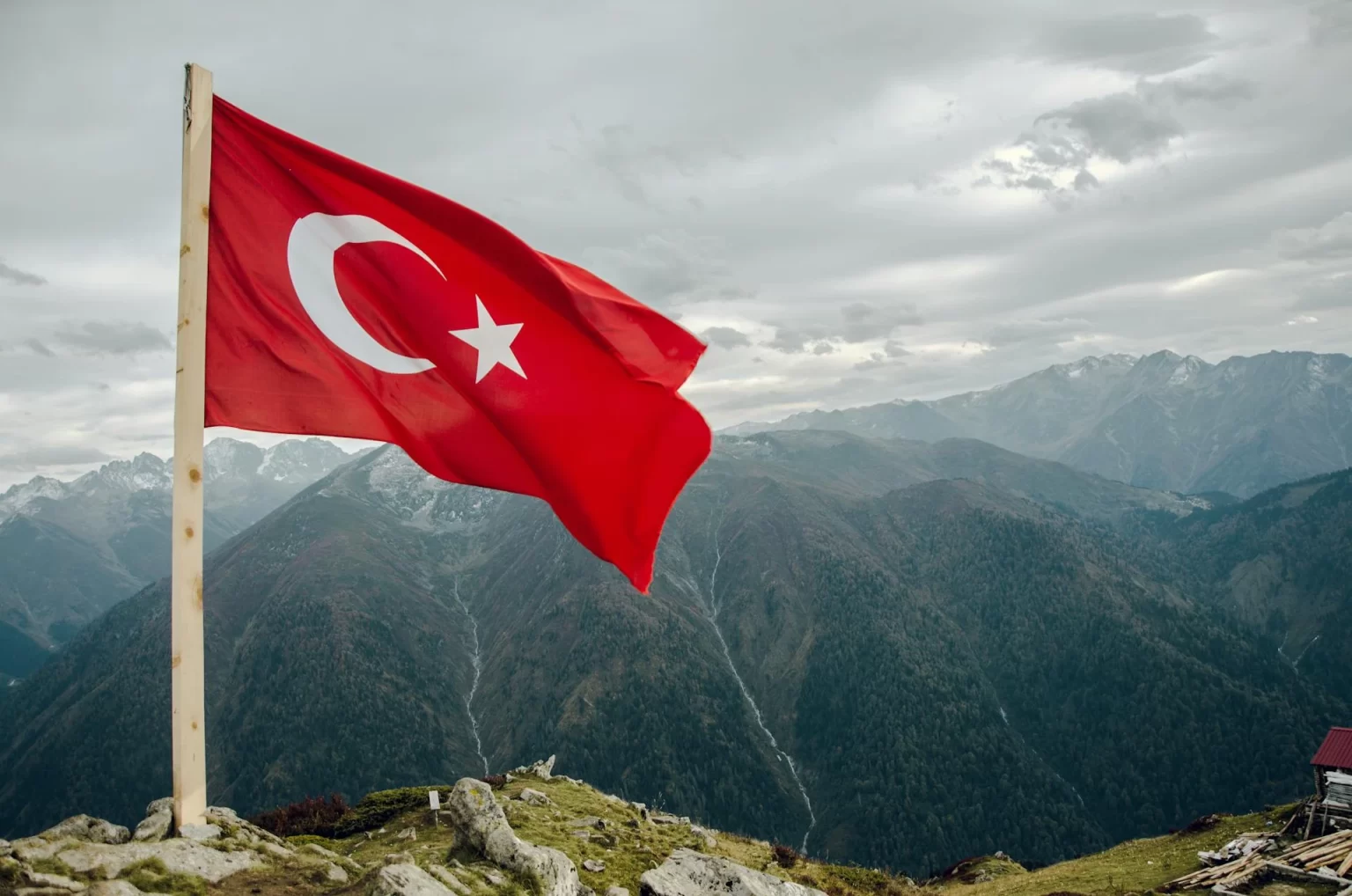 Turkish flag waving on a mountain overlooking a range of misty peaks.