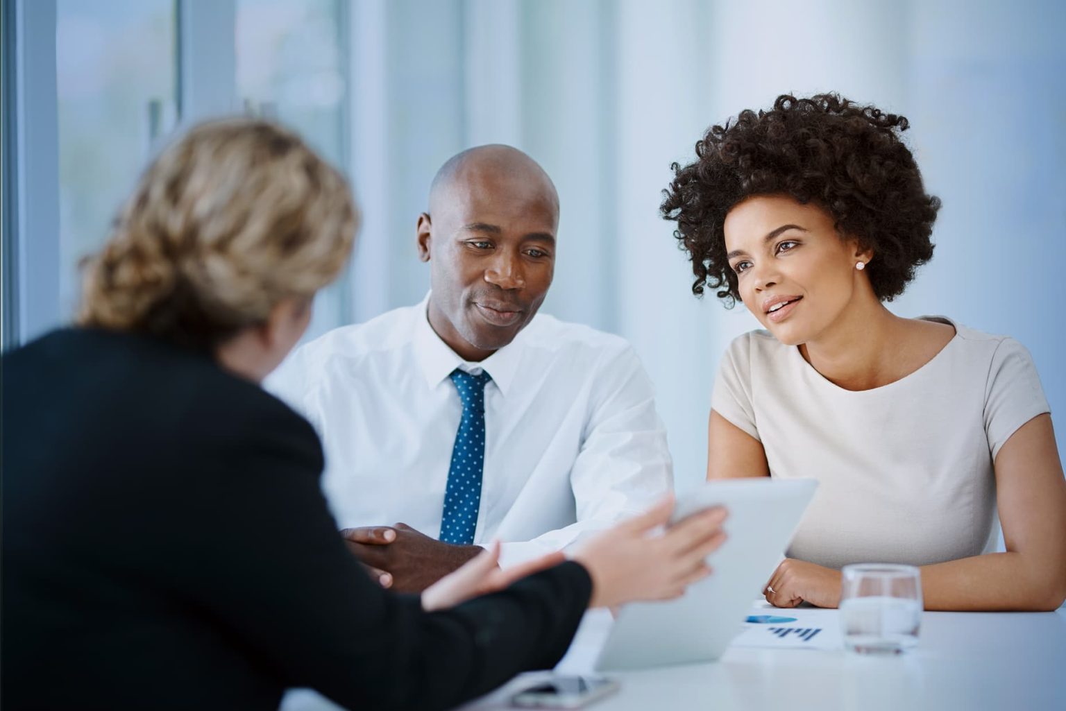 Three professionals in a meeting look at a laptop screen, engaged in discussion.