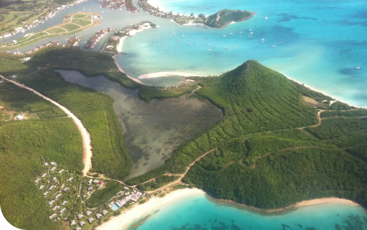 Aerial view of a coastal landscape with lush green hills, a heart-shaped lagoon, and turquoise waters.