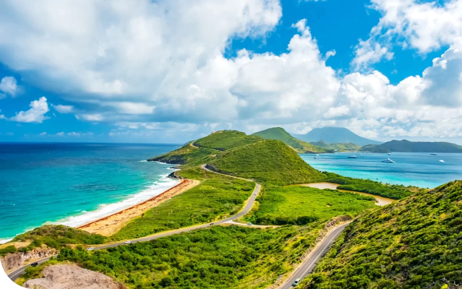 Lush green hills meet turquoise sea under a partly cloudy sky with a winding coastal road.