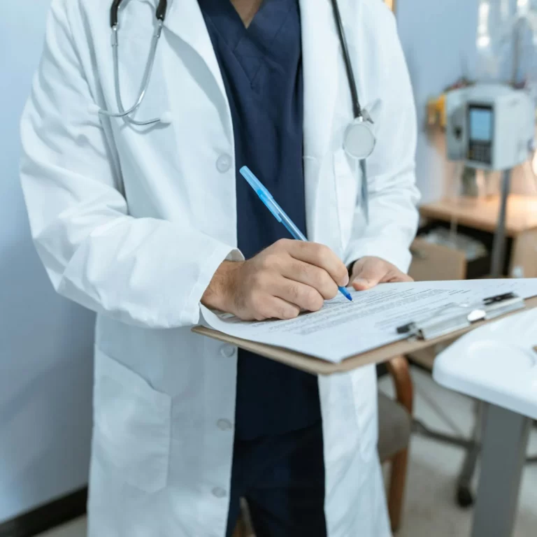 Doctor in a white coat writing on a clipboard in a medical office.