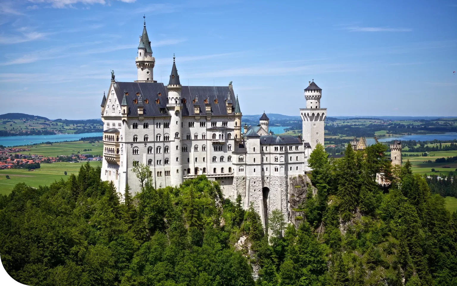 Neuschwanstein Castle perched on a forested hilltop under a clear blue sky.