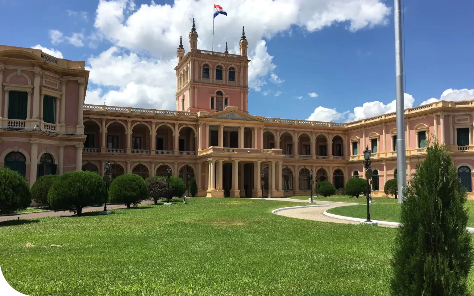 Palacio de los López with a flag on top, surrounded by lush green gardens under a blue sky.