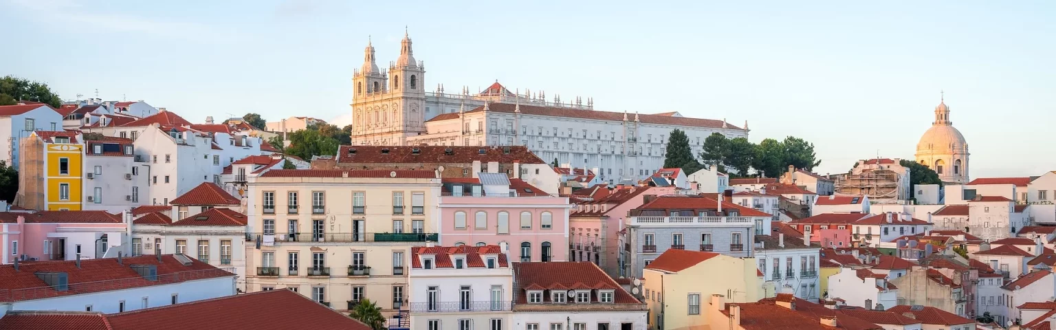 Colorful hillside view of Lisbon's rooftops with the Royal Palace and dome in the background at sunset.