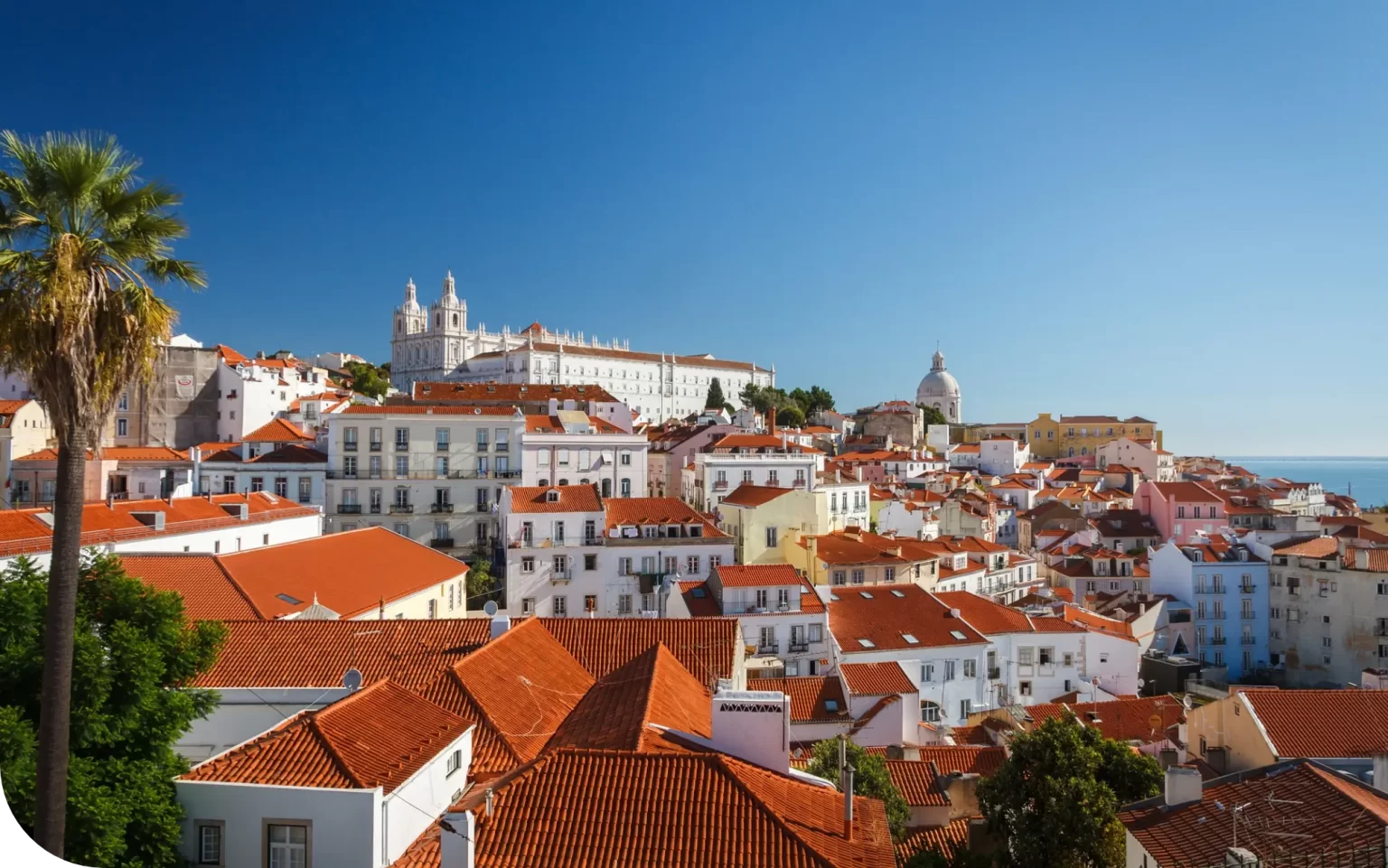 Lisbon's colorful hillside with terracotta rooftops under a clear blue sky.